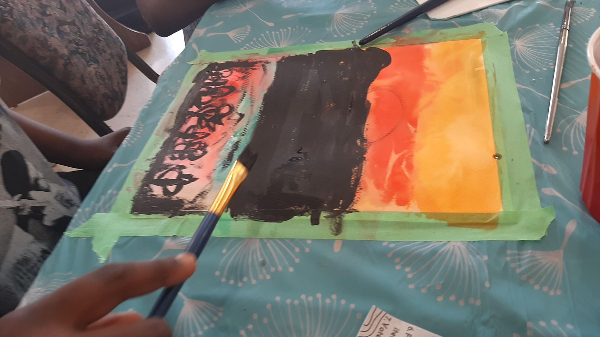 A person painting on a canvas with a paintbrush, using black paint on a colorful background.