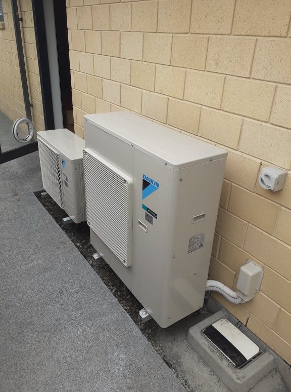 Daikin outdoor heat pump unit installed on brick wall.