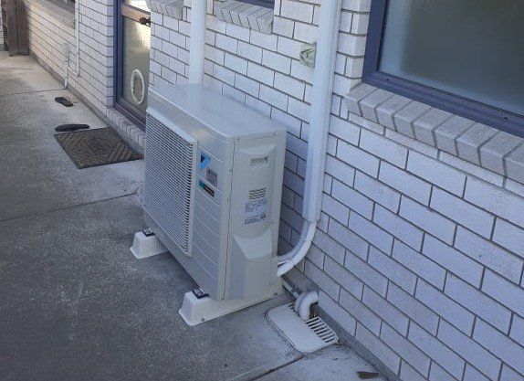 Daikin outdoor heat pump unit installed on brick wall.
