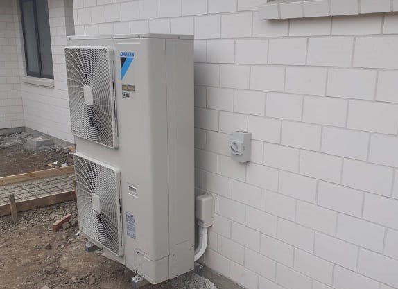 Daikin double fan outdoor heat pump unit installed on brick wall.