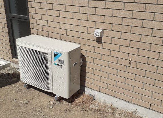 Daikin outdoor heat pump unit installed on brick wall.
