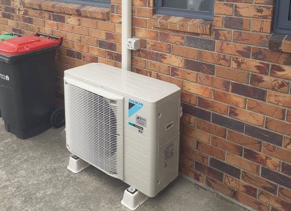 Daikin outdoor heat pump unit installed on brick wall.