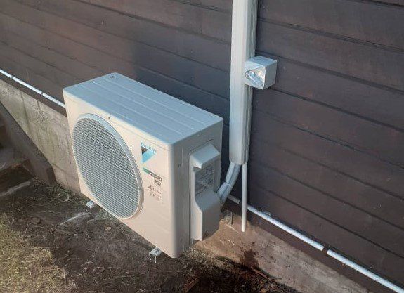 Outdoor heat  pump unit installed on black external wall.