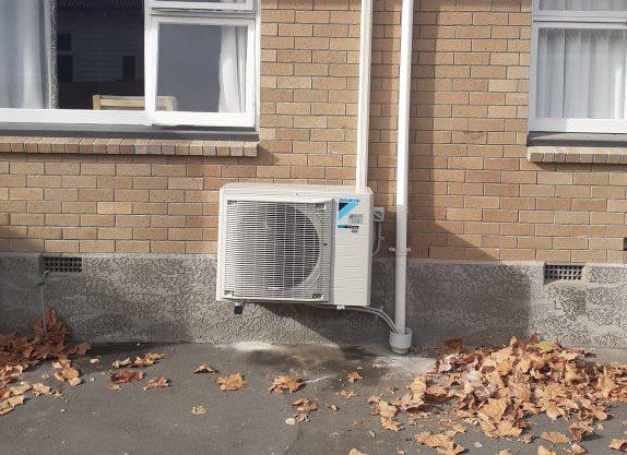 Installed Daikin heat pump outdoor unit on brackets, raised off the ground.