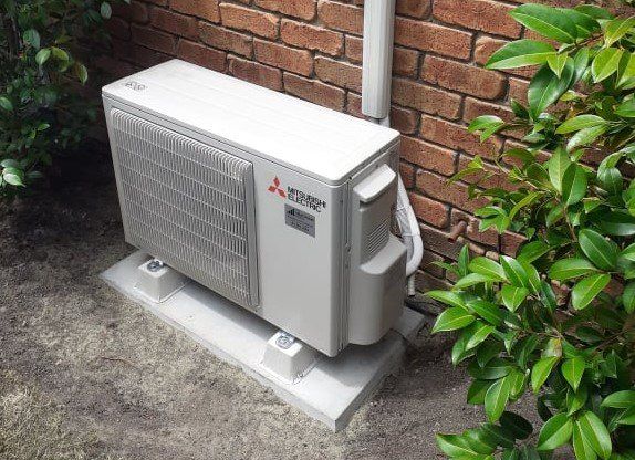 Mitsubishi Electric outdoor heat pump on concrete pad and feet.