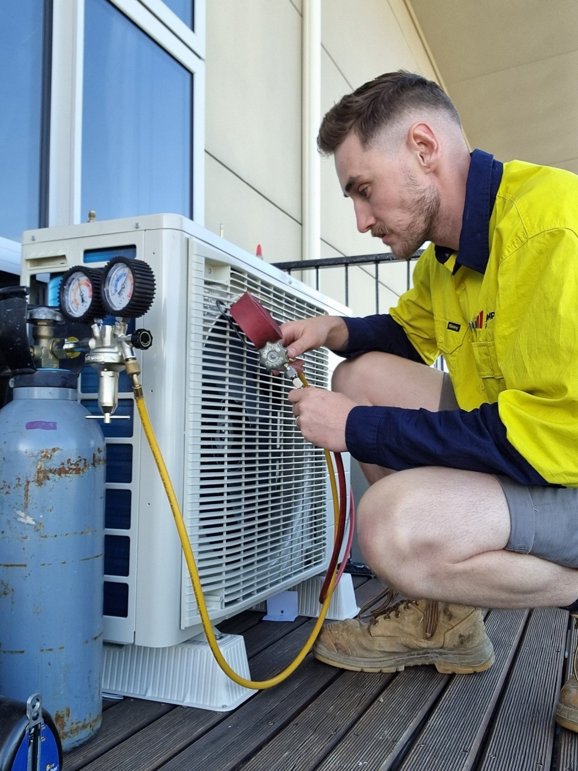 The Heat Pump People air conditioning technician with gauges checking outdoor heat pump unit
