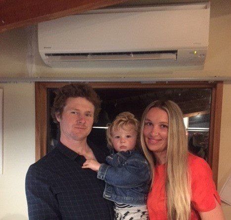 Family (man, woman and child) underneath a Daikin heat pump.