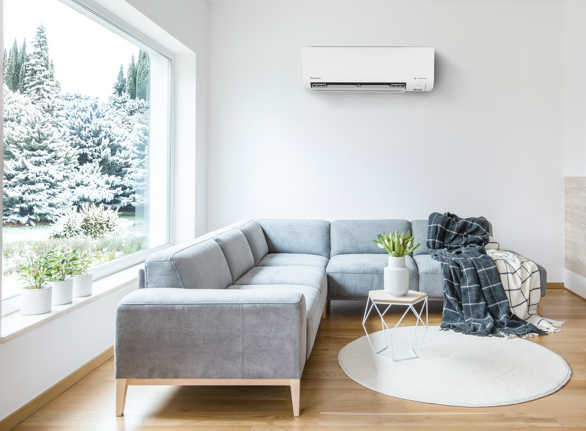 Daikin Alira X high wall heat pump in lounge with corner sofa and window looking out to snow covered trees.