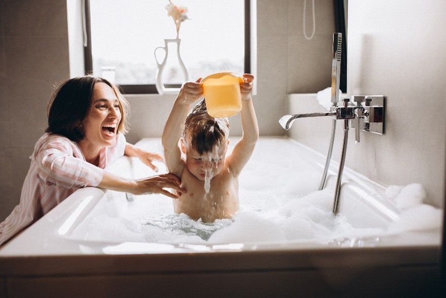 Mother bathing child in bubble bath. Child tipping water on head.