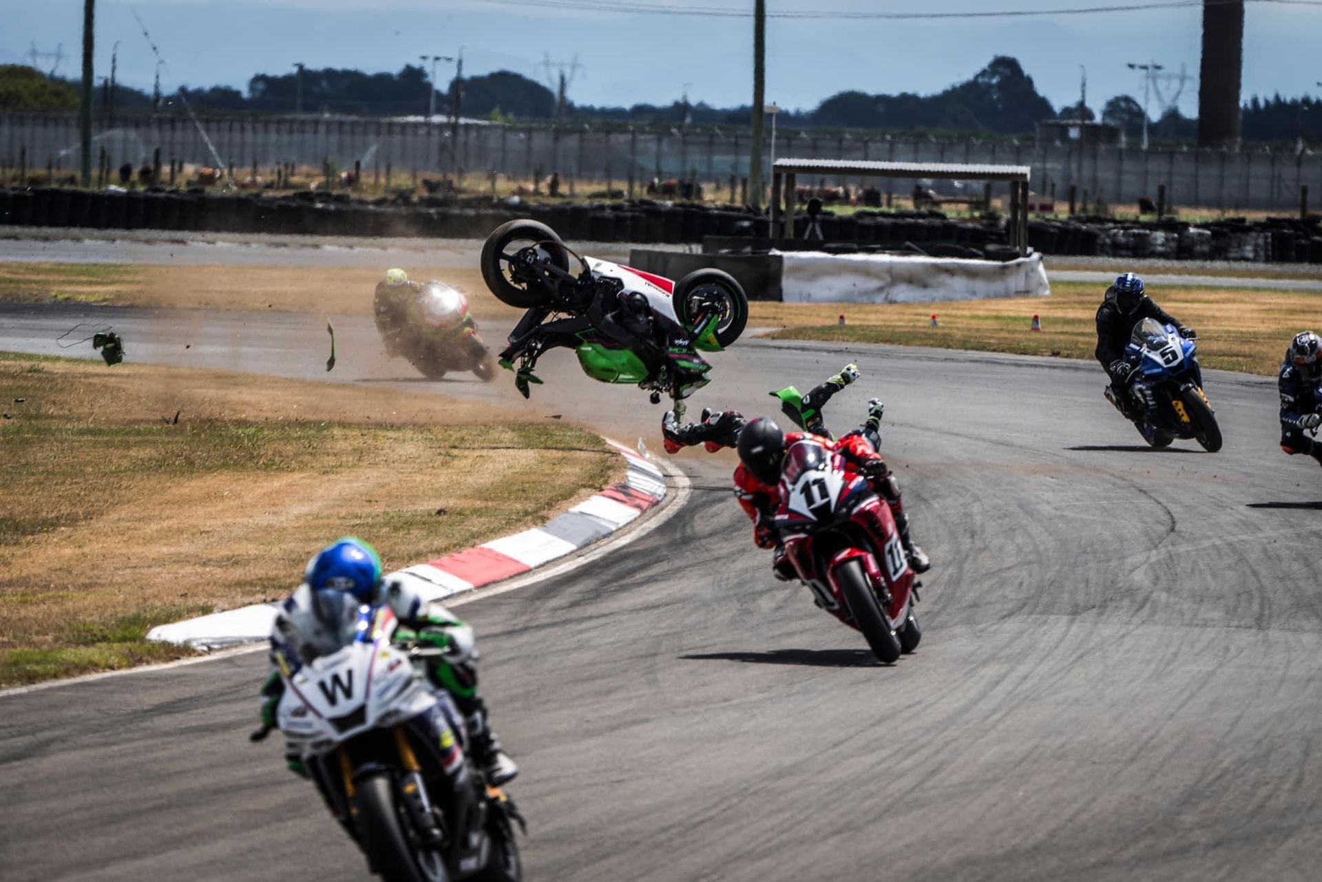 Dale Finch motorbike crash. Dale's motorbike flying through the air on the race track and Dale about to land on the track whilst motorbikes are racing.