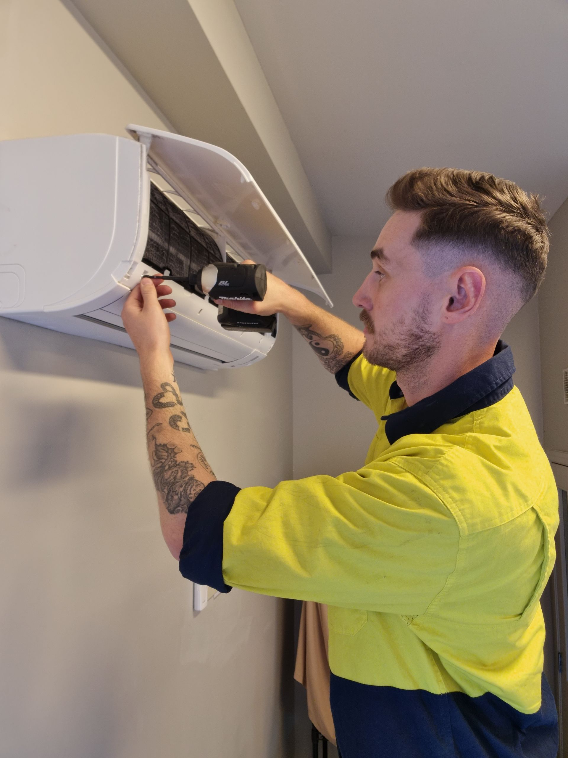 Air conditioning technician with drill removing heat pump filters from a high wall heat pump.