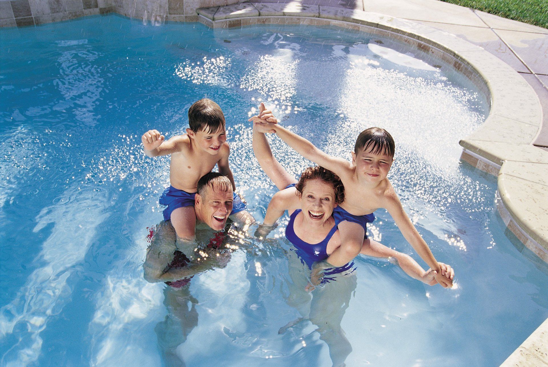 Family in residential swimming pool, happy, laughing together.