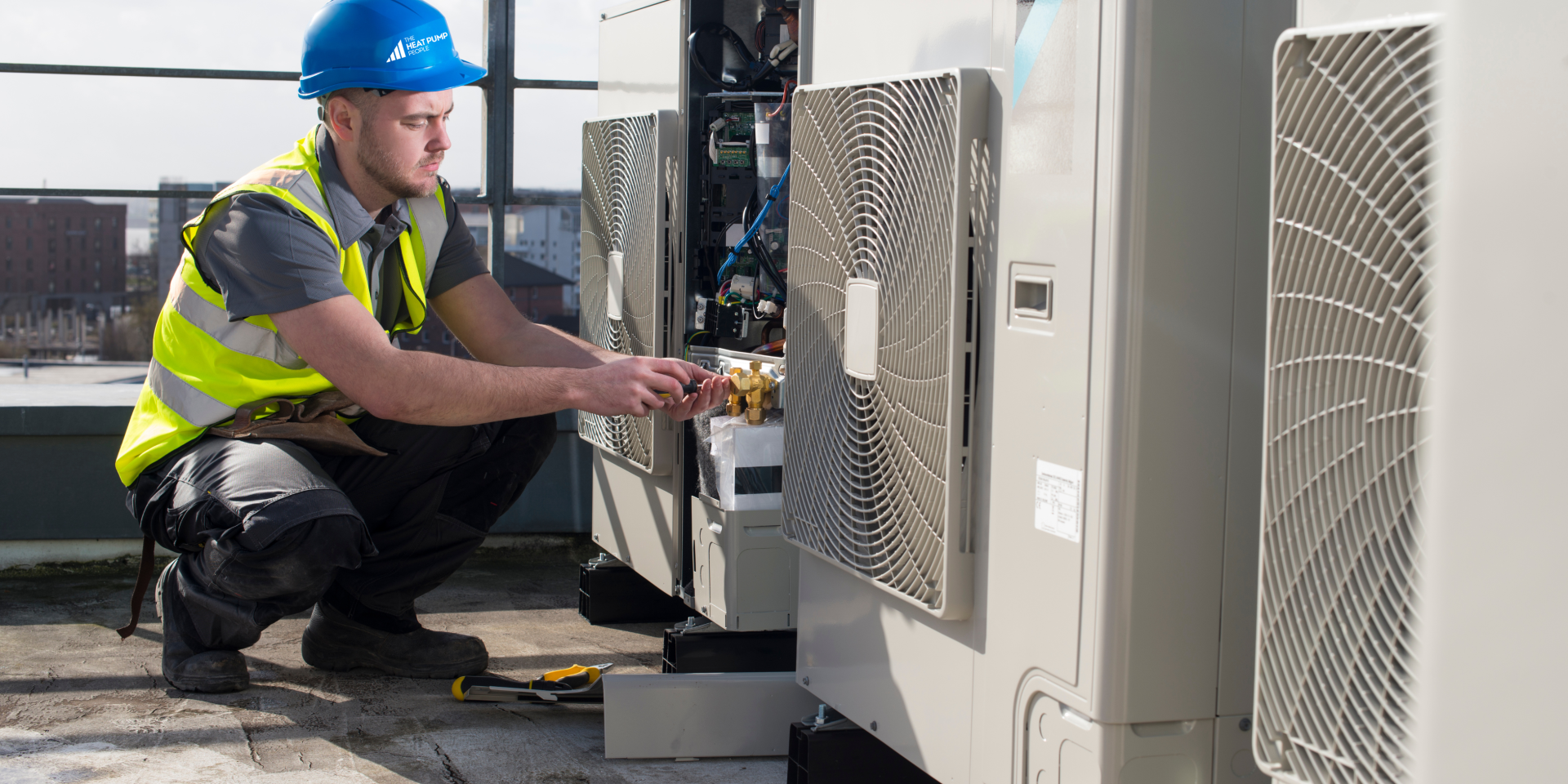 Air conditioning technician with hard hat and hi viz attending to outdoor commercial heat pump units on a roof top