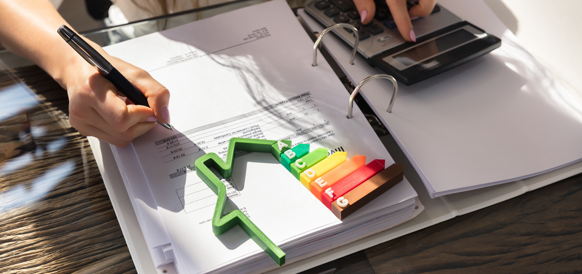 Woman's hands with calculator, pen, ring binder and energy saving symbol.