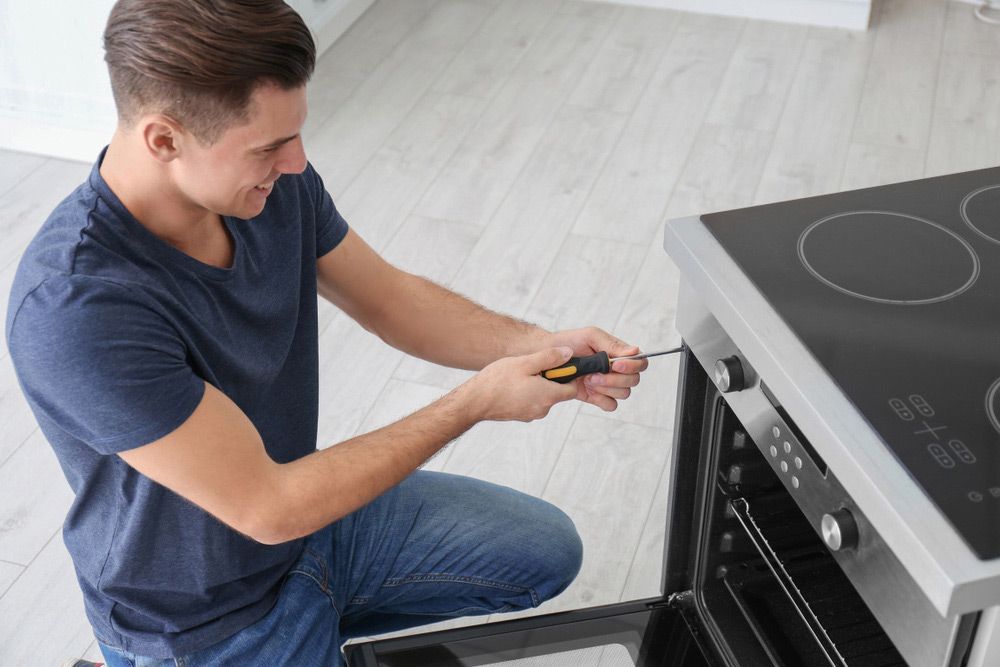 A Man is Fixing an Oven With a Screwdriver in a Kitchen — Bradmark Appliance Service in Garbutt, QLD