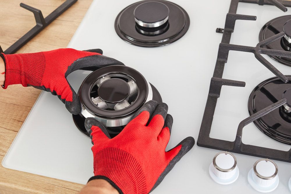 A Person Wearing Red Gloves is Fixing a Gas Stove Burner — Bradmark Appliance Service in Garbutt, QLD
