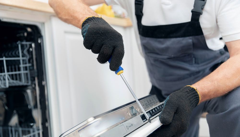 A Man is Fixing a Dishwasher With a Screwdriver — Bradmark Appliance Service in Garbutt, QLD