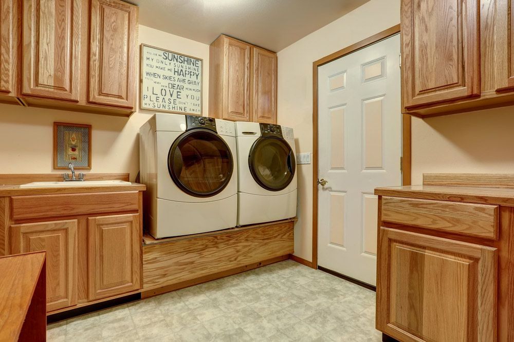 A Laundry Room With a Washer and Dryer and Wooden Cabinets — Bradmark Appliance Service in Garbutt, QLD