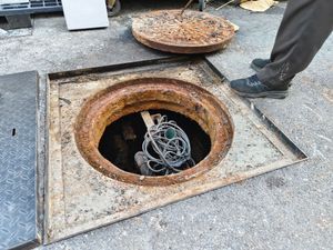 A manhole cover with a hose sticking out of it.