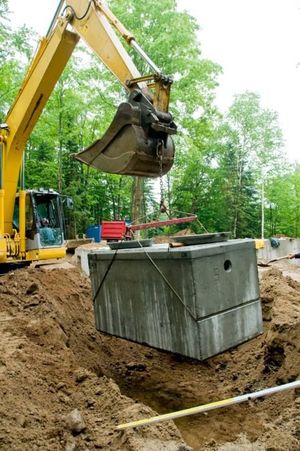 A yellow excavator is lifting a large concrete block into the ground.