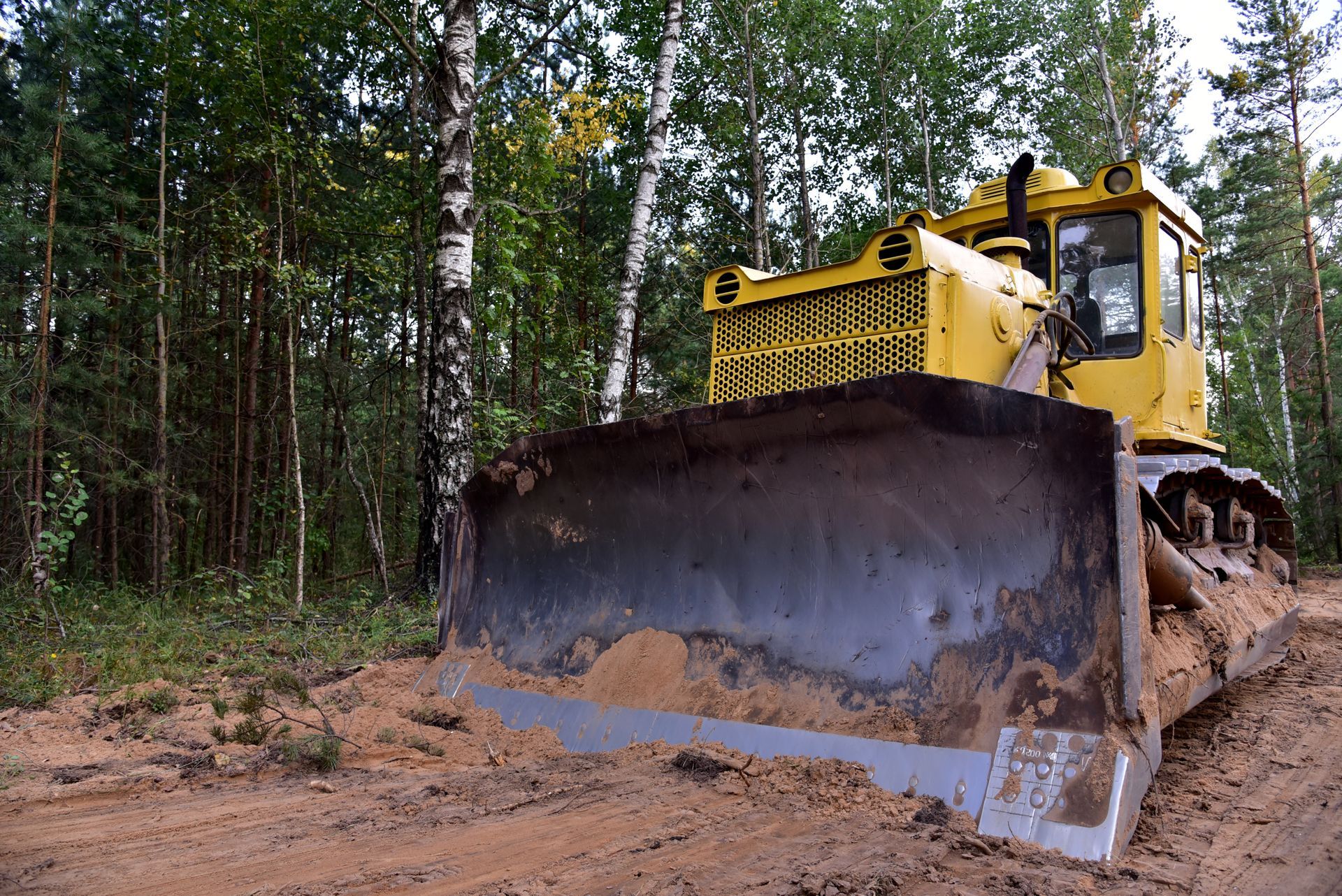 A bulldozer is driving down a dirt road in the woods.