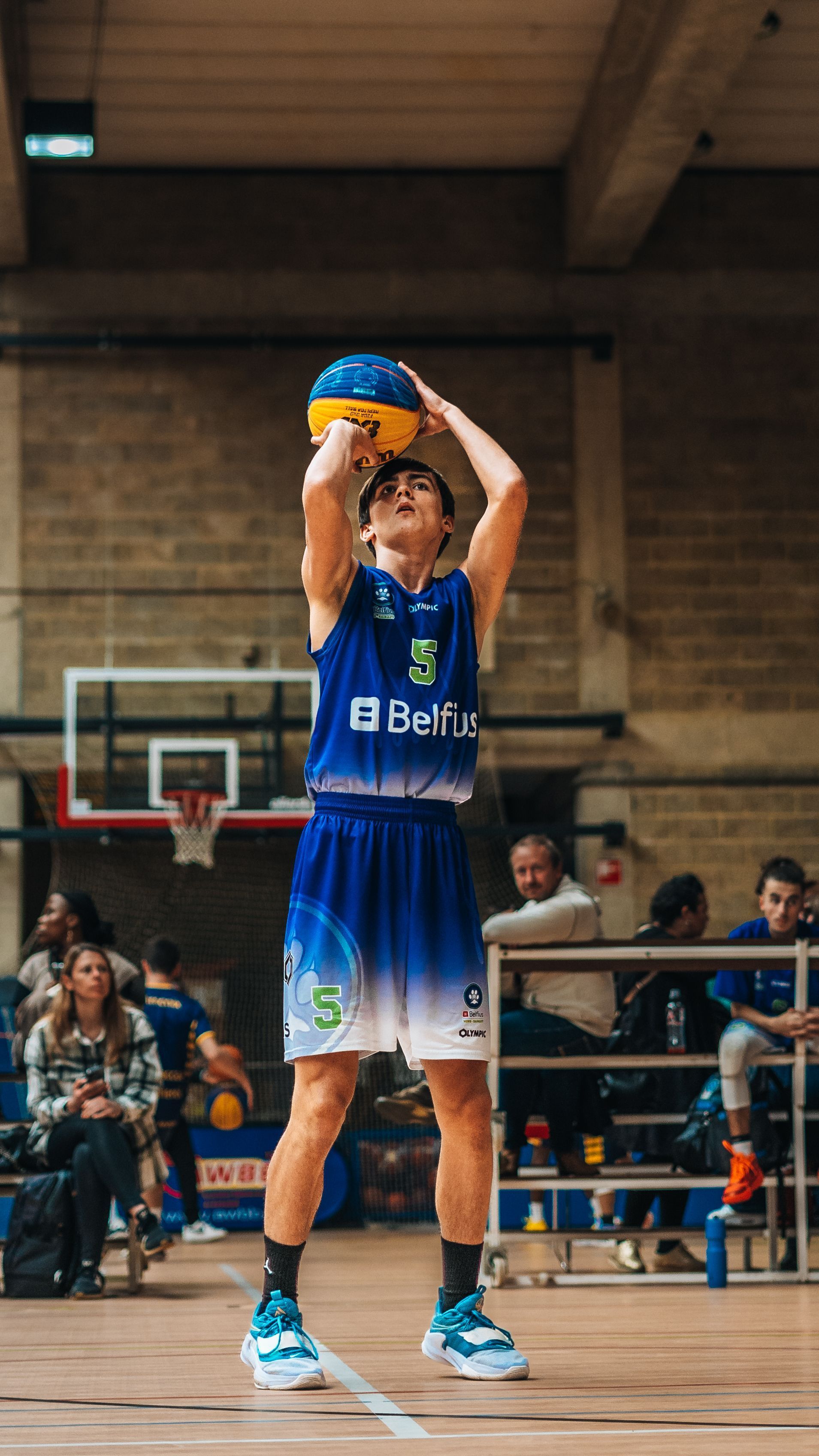 Basketball player in blue uniform holding a ball overhead on an indoor court