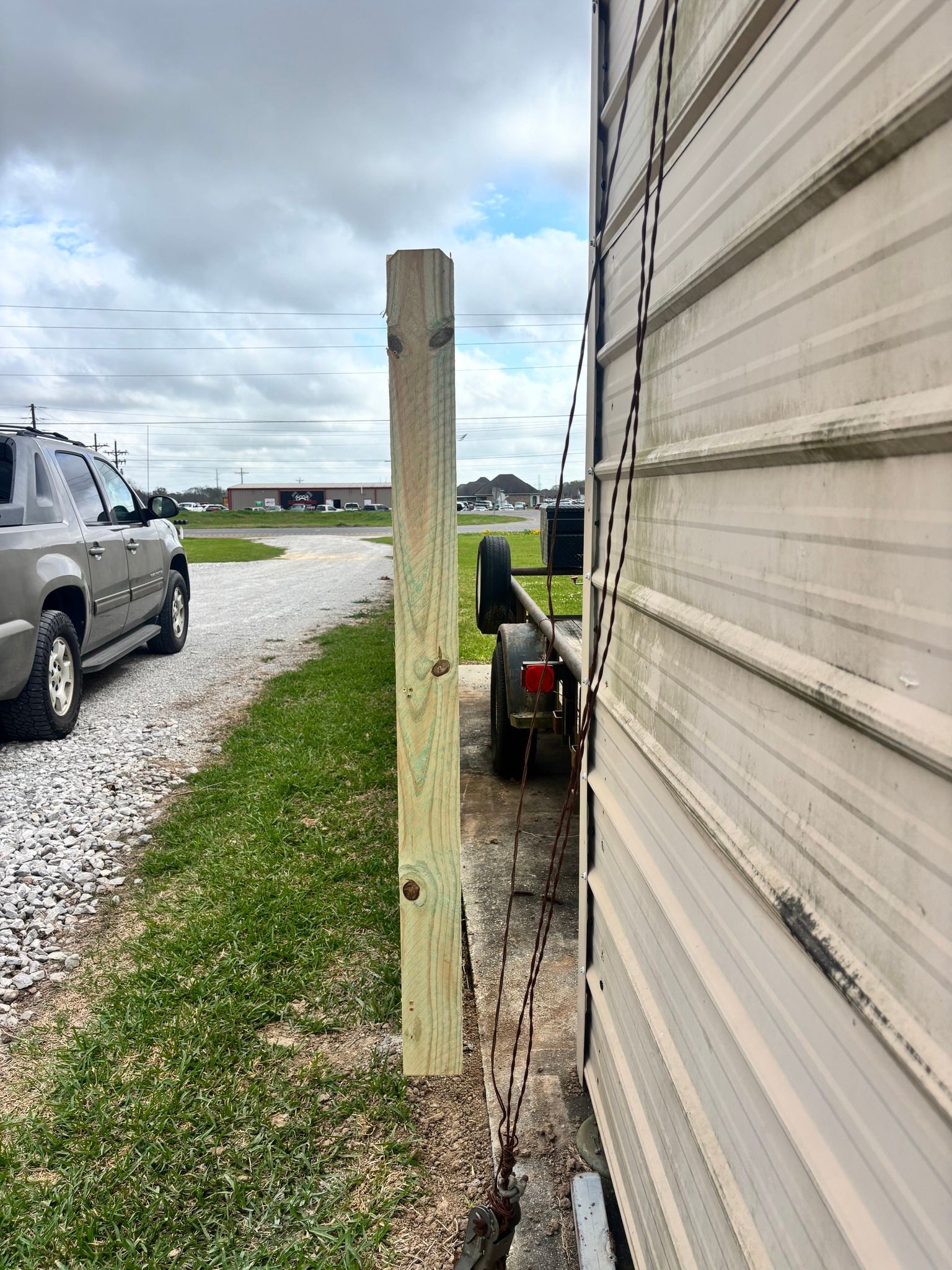 Gravel driveway beside a beige mobile home, with a wooden post and parked pickup under a cloudy sky.