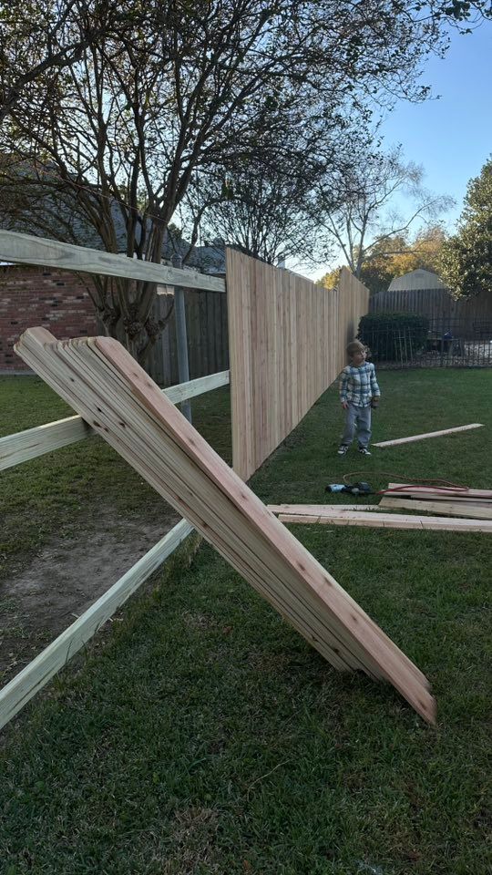 Wooden fence panels leaning in a yard, with a person standing near the partially built fence.