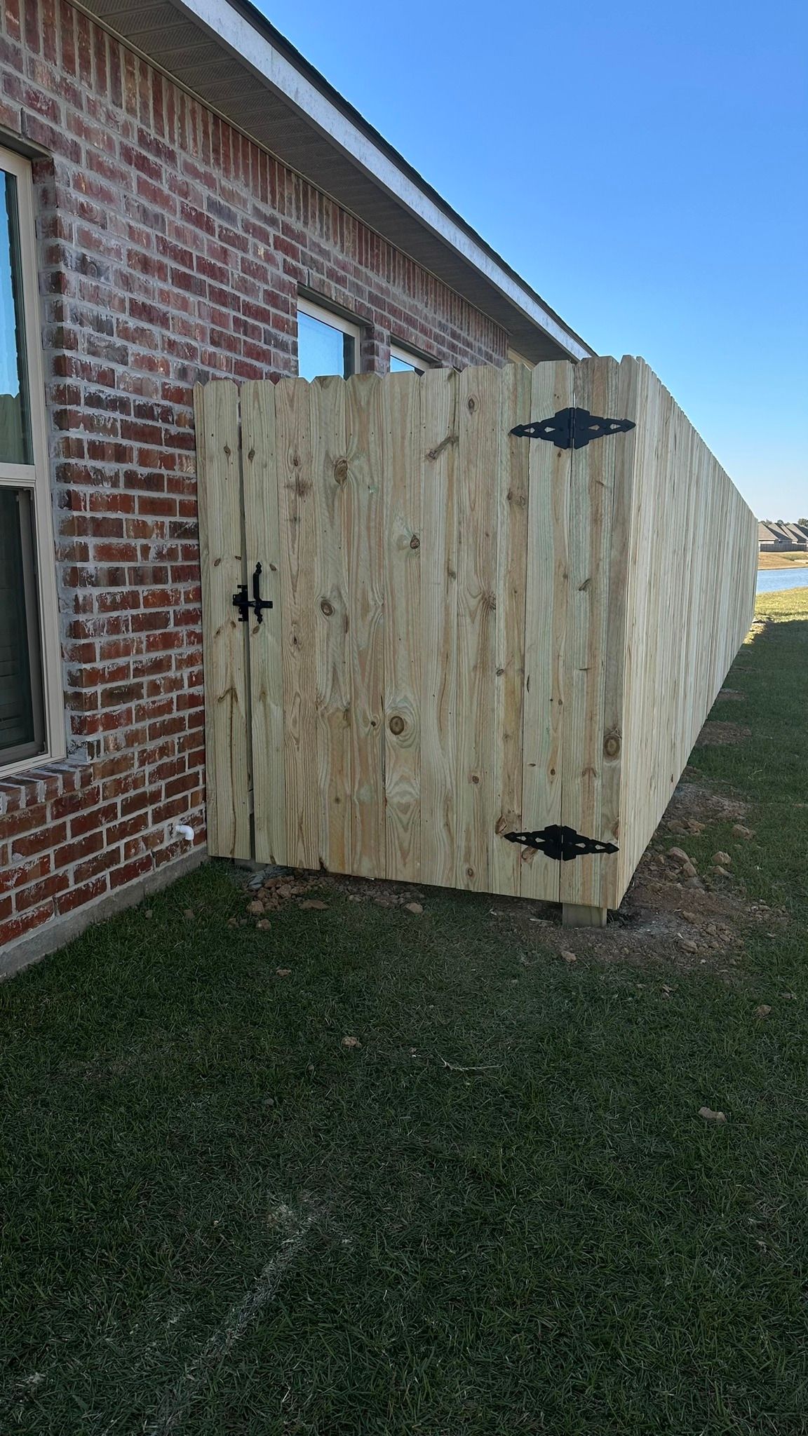 Wooden privacy gate beside a red brick building on a grassy lawn.