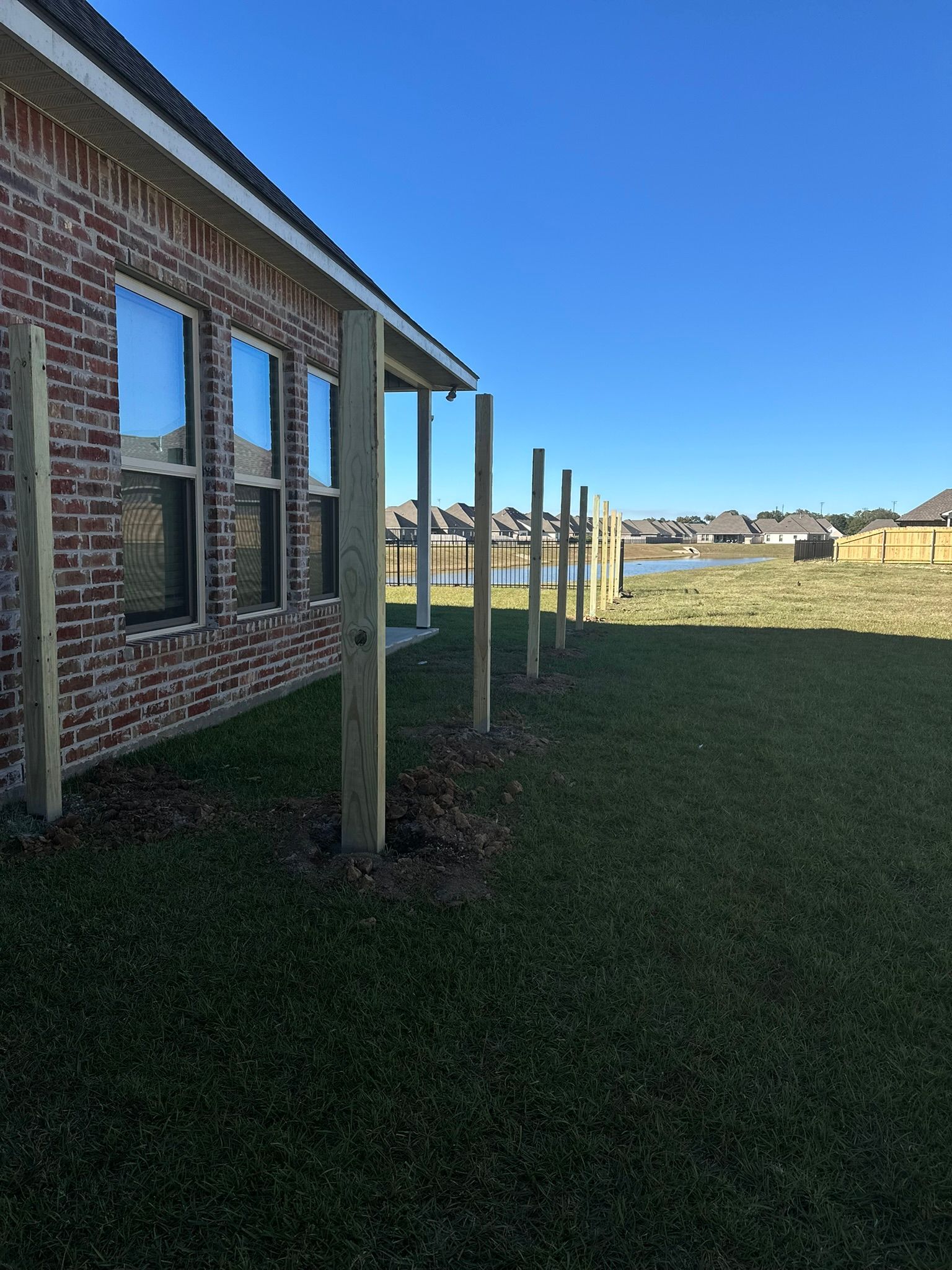 Brick house side yard with covered patio posts and a grassy lawn under a clear blue sky
