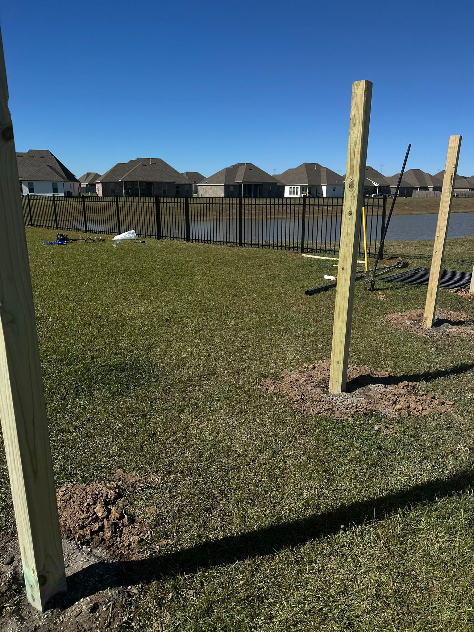 Backyard with wooden fence posts, grass, and suburban houses under a clear blue sky