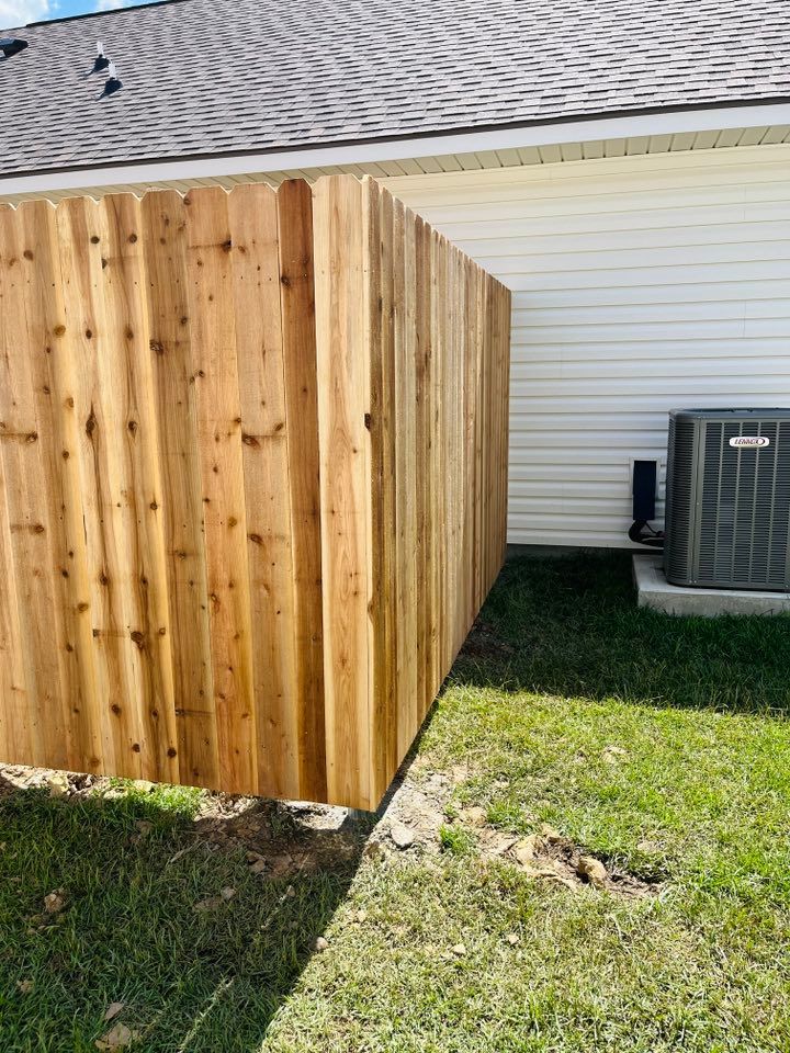 Wooden privacy fence beside a white house, with grass yard and HVAC unit.