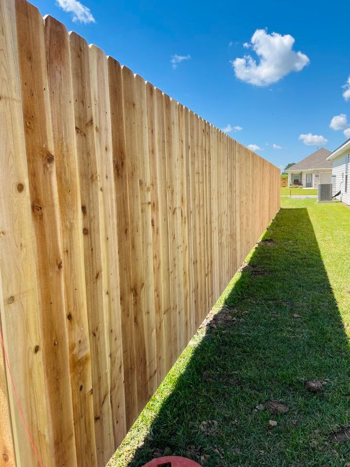 Tall wooden privacy fence beside a narrow grassy yard under a blue sky with clouds