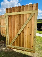 Wooden backyard fence gate with diagonal brace, set in grass under a blue sky