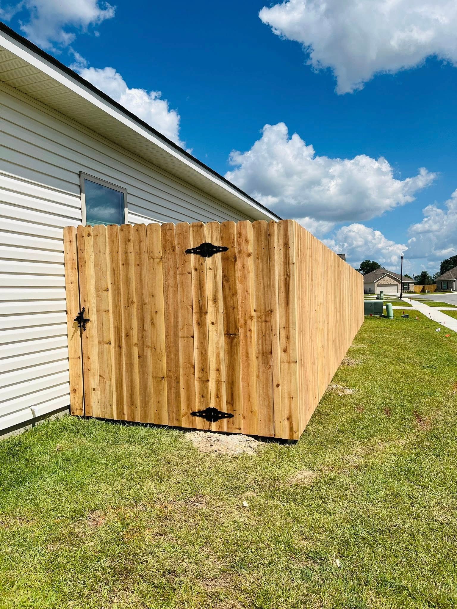 Wooden fenced enclosure beside a white house on a grassy lawn under a blue sky.