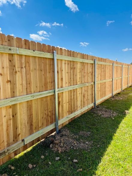 Wooden privacy fence along a grassy yard under a bright blue sky with clouds