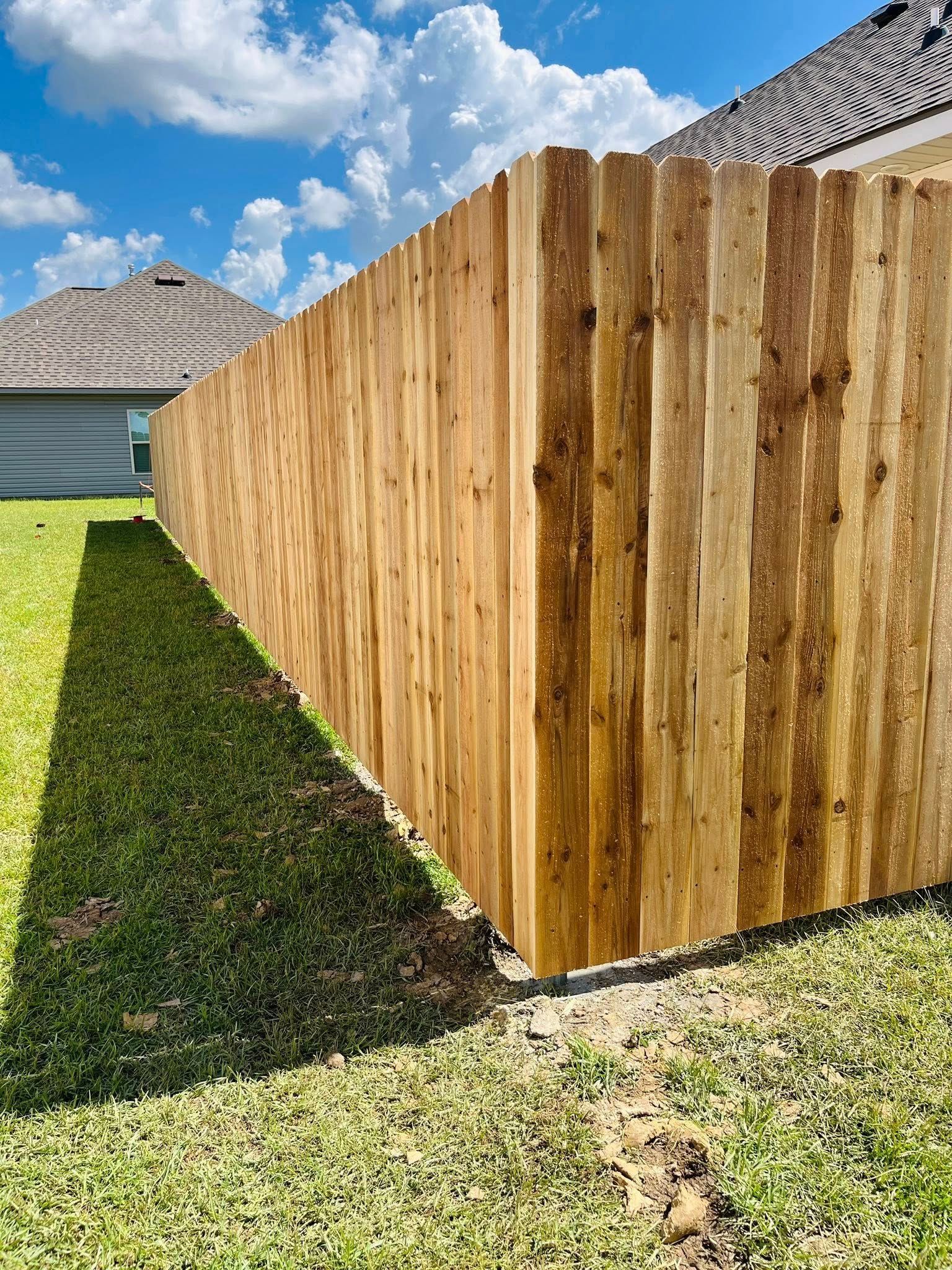 Wooden privacy fence along a grassy yard beside a house under a blue sky
