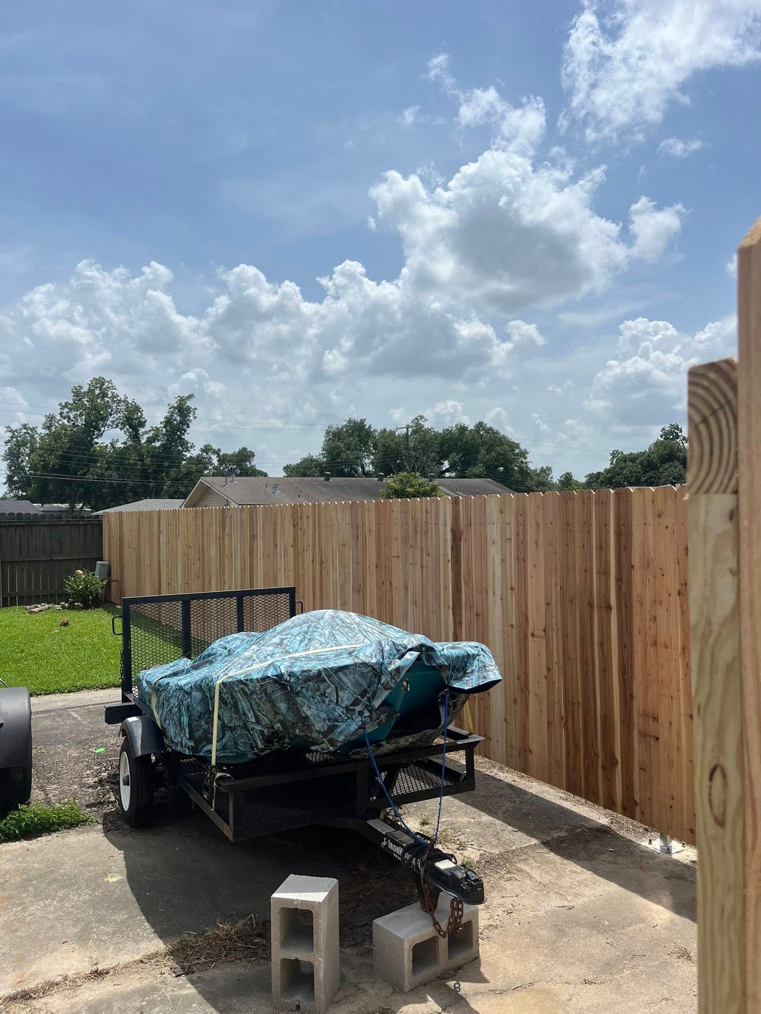 Utility trailer covered with blue tarp beside a wooden fence under a cloudy sky