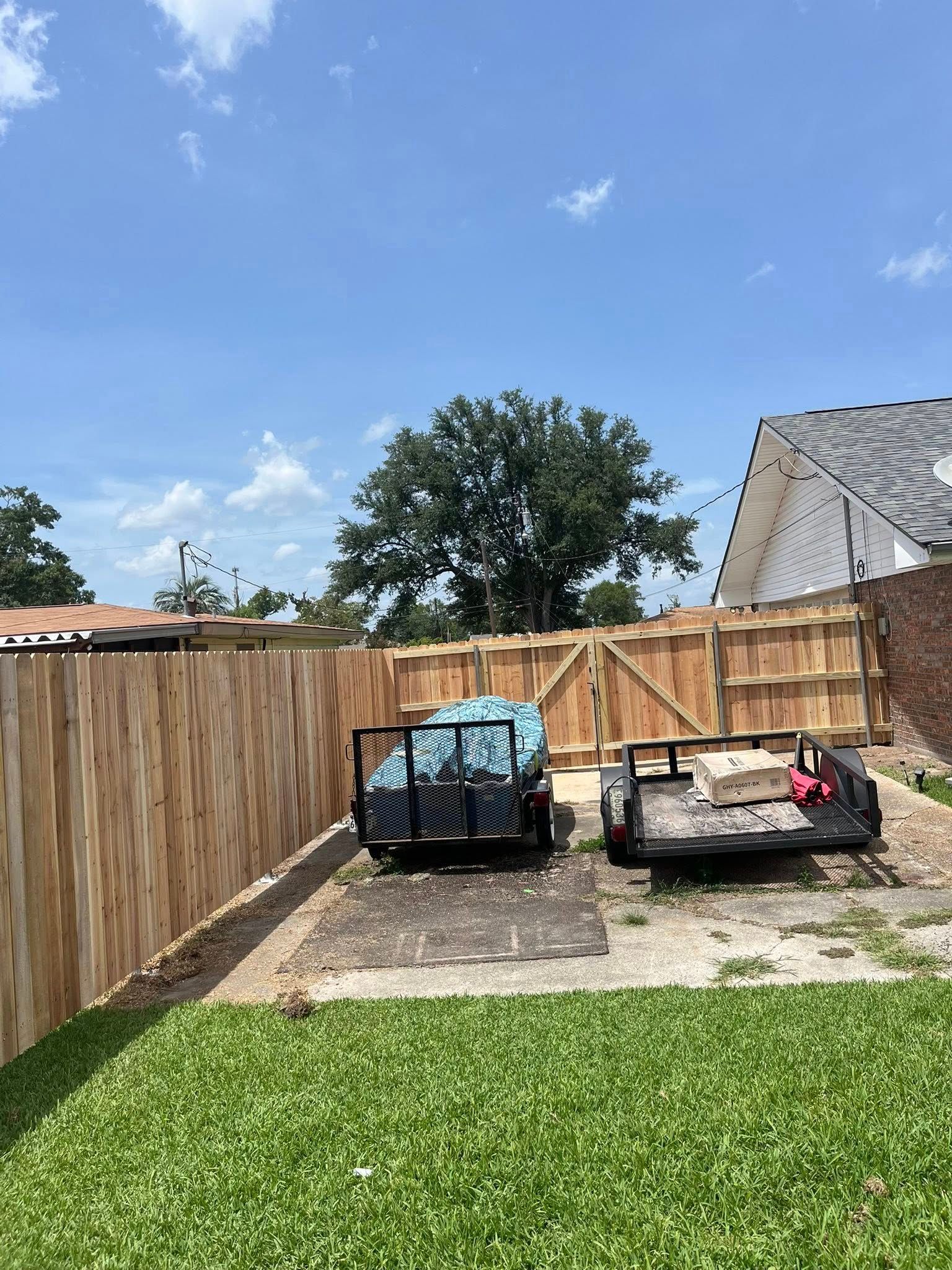 Backyard patio with two wicker sofas, wooden fence, green lawn, and blue sky