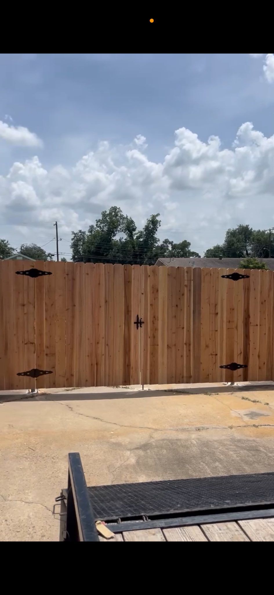 Backyard with a wooden fence, cloudy sky, and part of a trampoline in the foreground