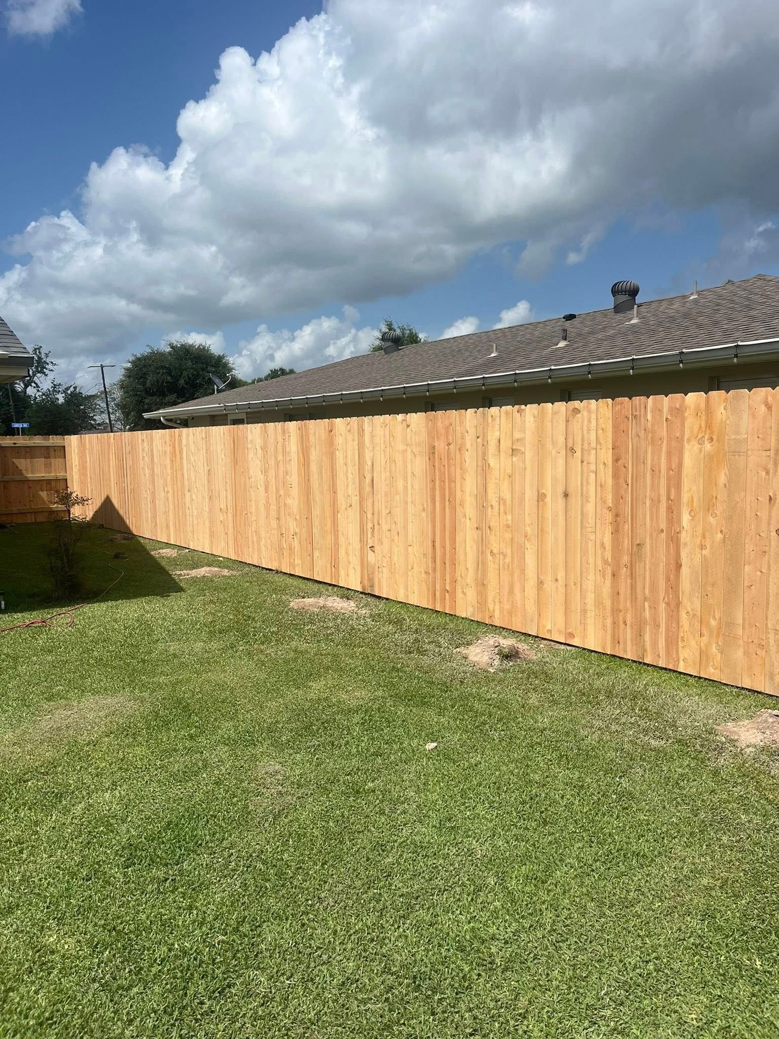 Backyard with a wooden fence, green lawn, and cloudy sky above neighboring rooftops