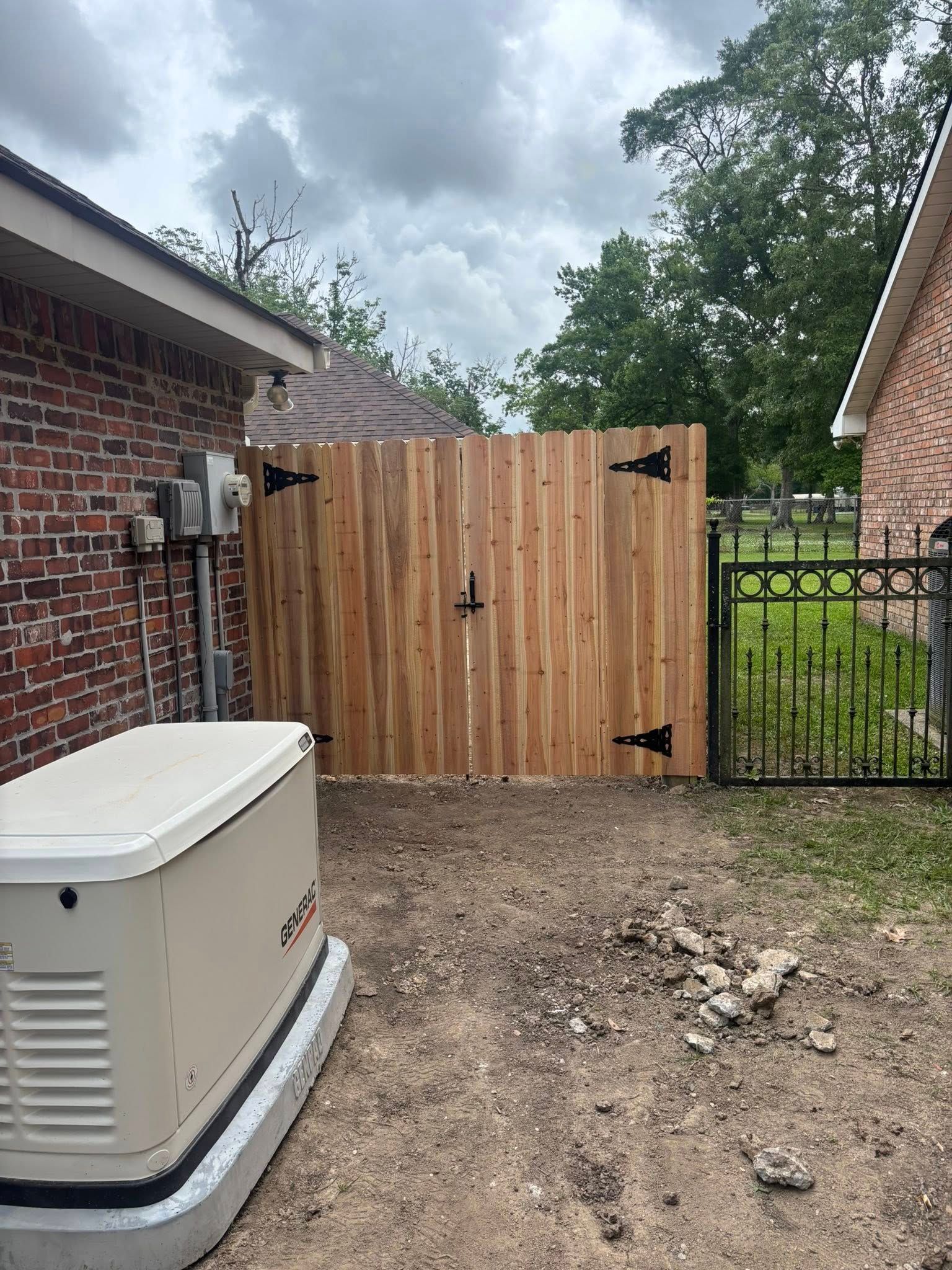 Wooden privacy gate beside a brick house, with a gravel yard and gate latch visible.