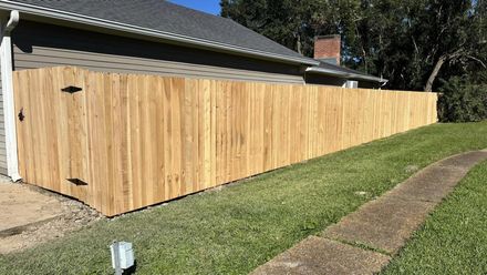 Wooden fence along a grassy yard beside a concrete path and house roofline