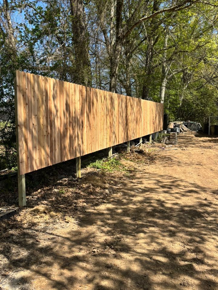 Wooden fence panels along a wooded dirt path in sunlight
