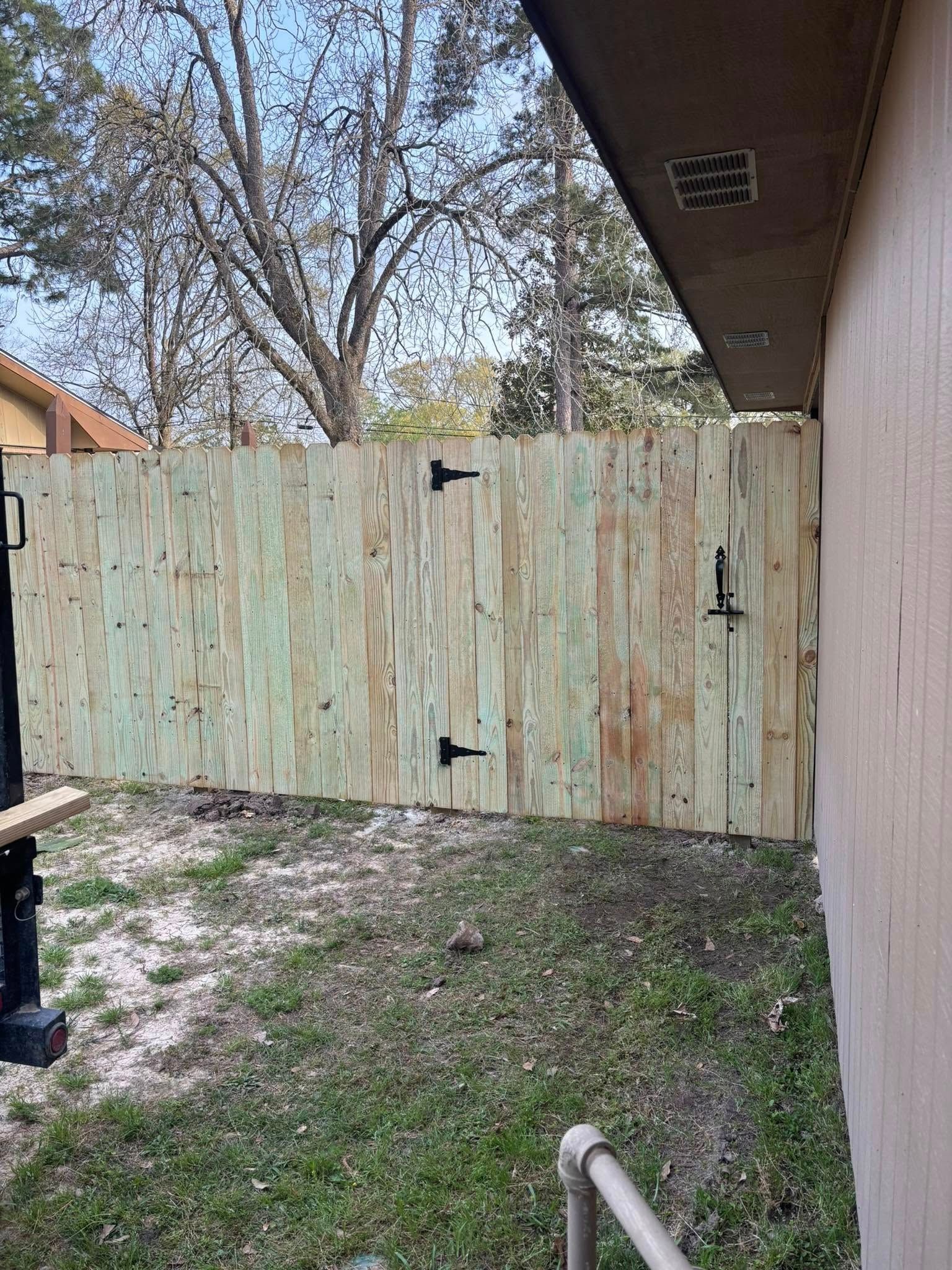 Weathered wooden fence and gate in a small dirt-and-grass side yard beside a house