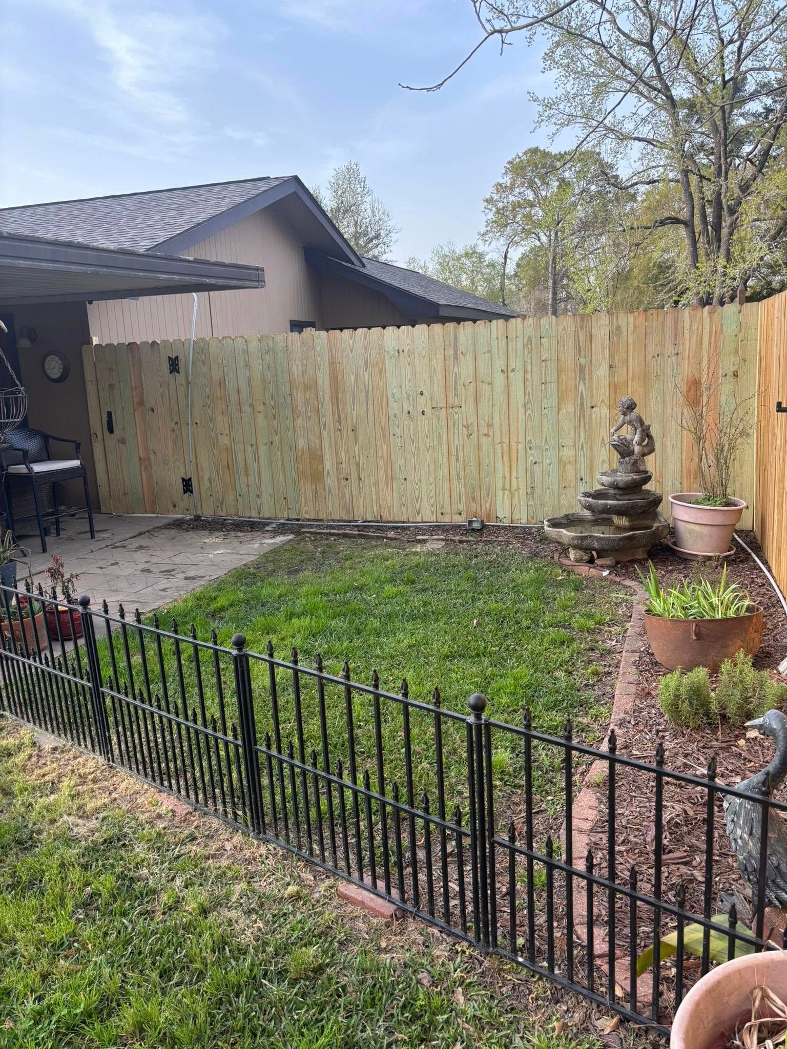 Backyard garden with black fence, wooden privacy fence, stone fountain, and house patio view.