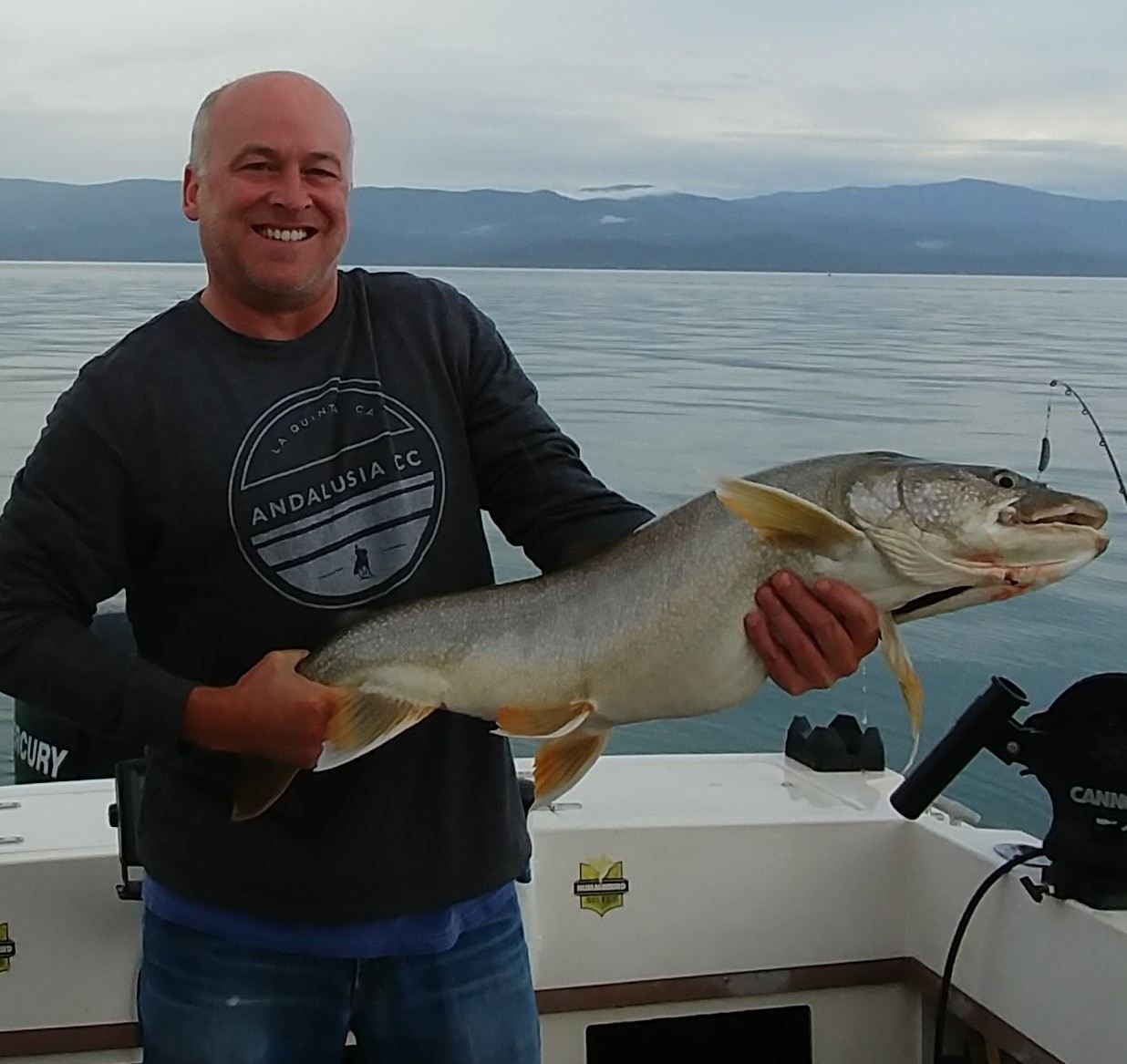 A man holding a large fish wearing a shirt that says anchorage on it