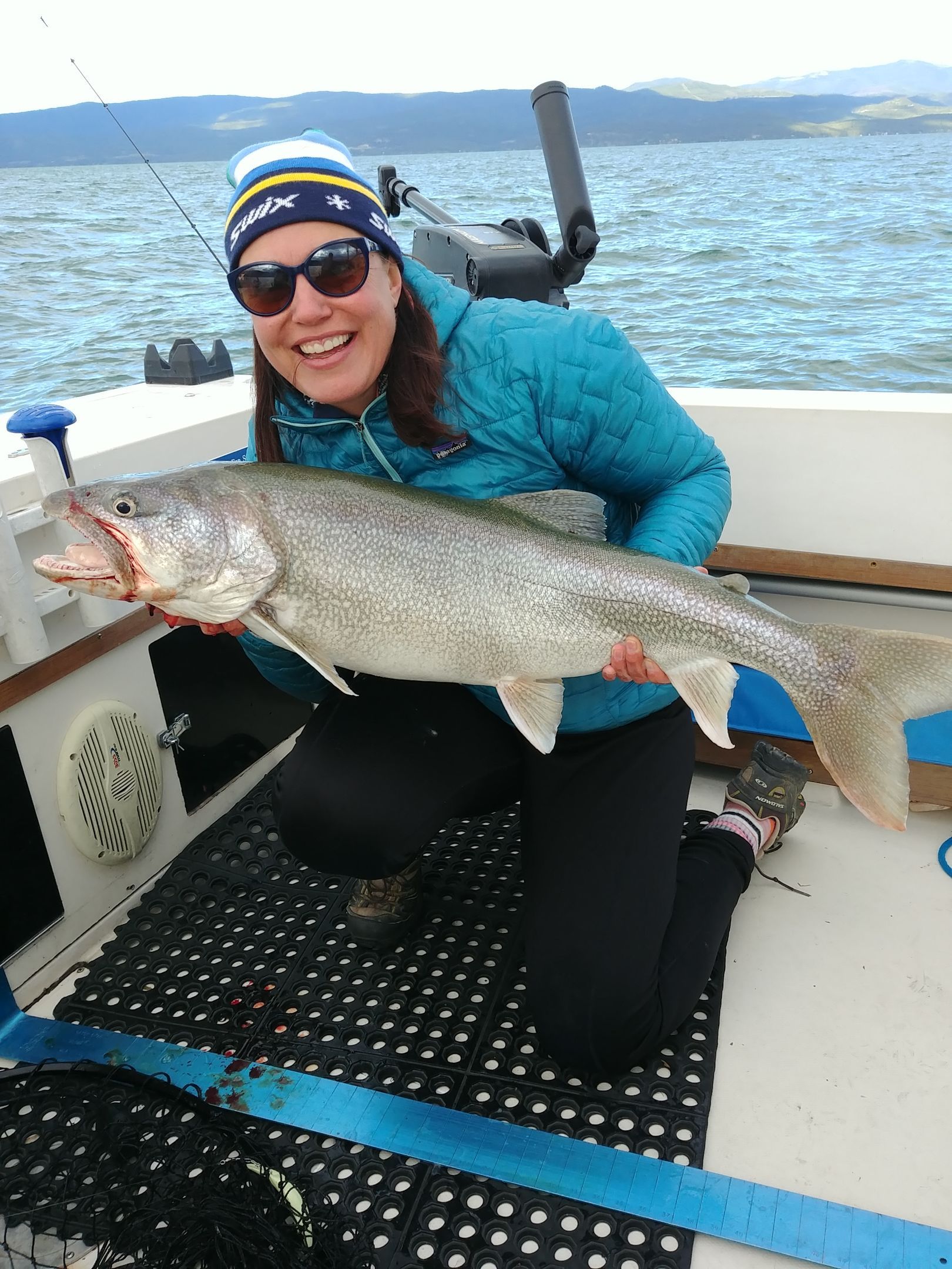 A woman is kneeling on a boat holding a large fish.