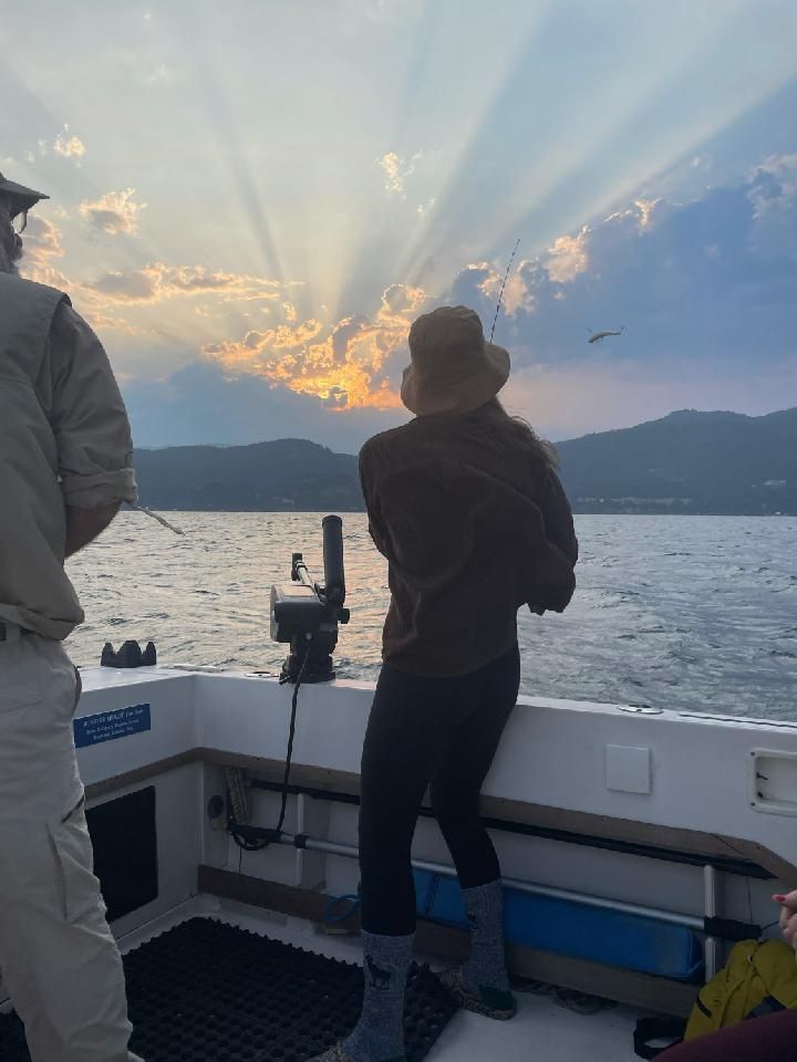 A man and a woman are standing on a boat looking at the sunset.