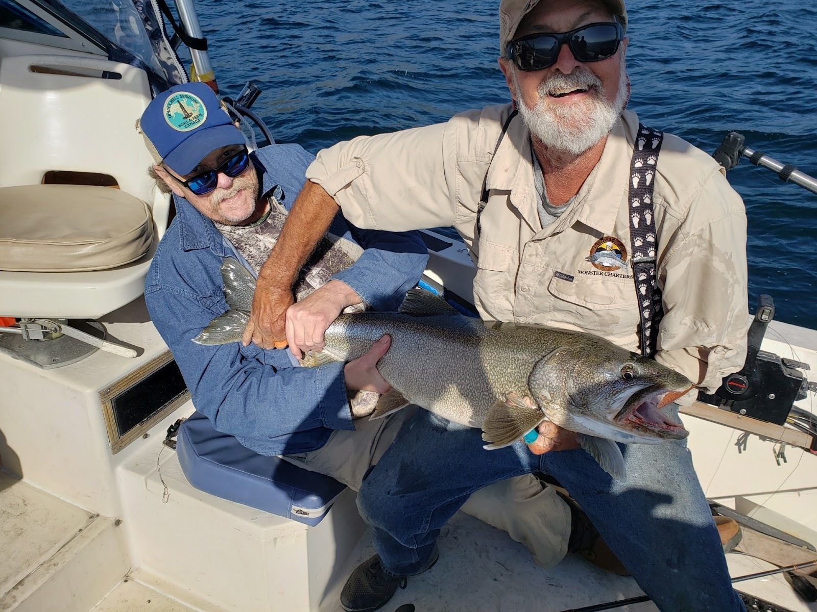 Two men are sitting on a boat holding a large fish.